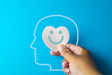 Hand holding a heart-shaped smile inside a head outline idea for Emotional health,mental health,emotional well-being,mental wellness, and self-care awareness.