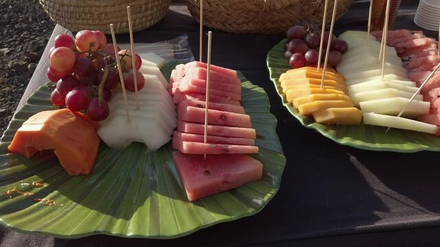 Colorful arrangement of watermelon, melon, papaya, mango, and grapes, served on green leaf shaped platters, creating a visually appealing tropical fruit display