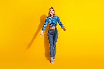 Blonde woman in casual stylish outfit standing against vibrant yellow background expressing happiness with open arms