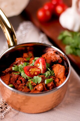 Spicy Liver Curry garnished with tomato and cilantro served in a copper bowl on a rustic table side view of Indian meat dish