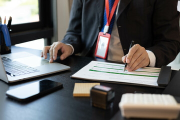 A man in a suit is working on documents in an office. He holds a pen and is analyzing data. This scene conveys a professional working atmosphere.
