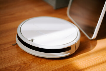 Robot vacuum cleaner on wooden floor during daytime, efficiently navigating and cleaning dust and debris