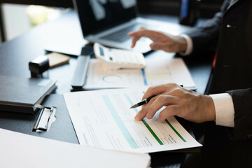 A man in a suit is looking at a piece of paper with graphs on it. He is holding a pen and he is analyzing the data. The scene suggests a professional setting
