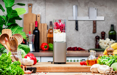 Healthy vegan eating, cooking, food blogging banner background with blender with bananas, raspberries and vegan milk for smoothies on wooden board on cozy kitchen with wooden table, kitchenware 