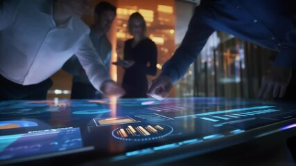 Business team working late at night analyzing financial data on a futuristic interactive touchscreen table in a high tech control room with server racks in the background - Powered by Adobe