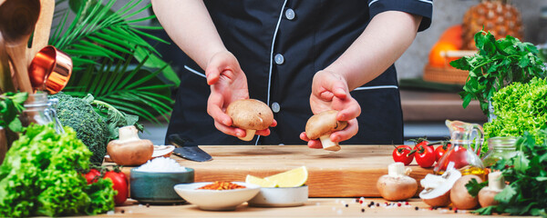 Chef showing fresh organic brown mushrooms from farm market. Cozy kitchen with wooden table, kitchenware, vegetables, herbs and ingredients for cooking. Healthy vegan food, culinary, recipes
