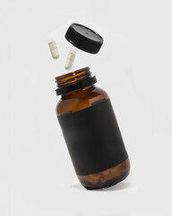 Amber pill bottle with blank black label on white background with pills and lid floating