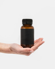Woman's hand holding amber supplement bottle on white background
