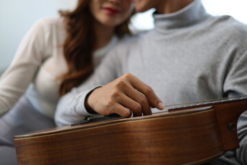 A young man and woman, a couple, relax on a comfortable sofa in a new apartment or house. Happy Asian couple relaxing happily playing guitar on sofa in living room.