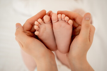 the baby's small feet in her mother's arms, the mother gently strokes the legs or heels of a newborn baby, maternal love and care