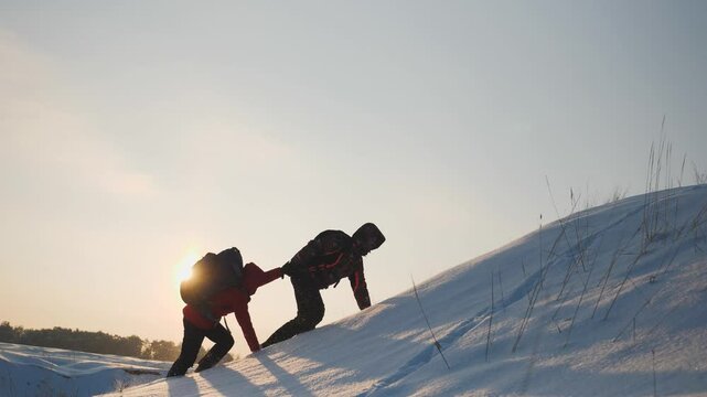 climbers climb snowy mountain sunset winter. teamwork concept. overcoming obstacles together. give helping hand. business teamwork silhouette. hiking path mountains. success active sports backpacks