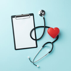 Red heart with doctor stethoscope and tablet on blue background. Copy space. Top view.