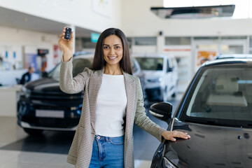 Happy young woman bought car in dealership center, smiling millennial female posing with keys in...