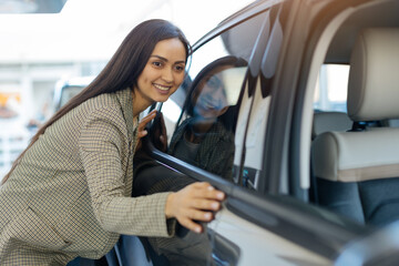 Happy woman embracing her new car with excitement inside modern dealership showroom. The polished...