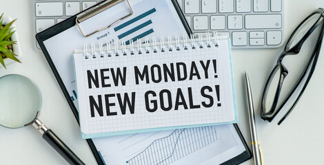 A notebook with a spiral binding and a pen on top of it with the words New Monday. New Goals...