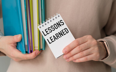 A person is holding a notebook with the word Lessons Learned written on it