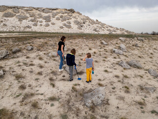 A mother and her two sons searching for treasures in a sandy outdoor area using a metal detector...