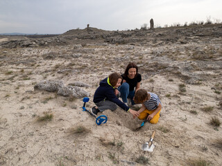 A mother and her two sons searching for treasures in a sandy outdoor area using a metal detector...