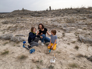 A mother and her two sons searching for treasures in a sandy outdoor area using a metal detector...