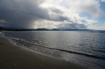 Glistening waves lap against the shore beneath a dramatic sky reflecting on tranquil waters