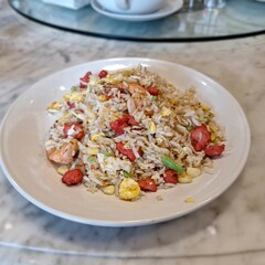 Indonesian-style fried rice (Nasi Goreng) with egg, shrimp, chicken, and green beans, presented on a plate over a marble surface.
