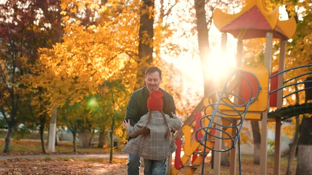Young father extends arms to lift little daughter during walk in park. Positive father and daughter in own world of happiness at sunset. Father appreciates every day spending with lovely daughter