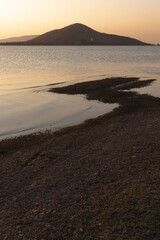 Pa Sak Jolasid Dam, Serene Coastal Sunset: A tranquil view of an island at dusk, with a silhouette of hills and serene water reflecting the warm colors of the setting sun, creating a peaceful