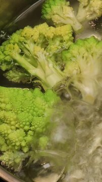 green romanesco broccoli cooking in boiling water, close-up view. romanescu broccoli florets being boiled in pot. concept, healthy eating, nutrition, cooking. food, recipe books