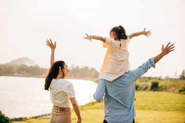 Asian family child girl piggyback riding back on father raising hands like flying outdoor nature...