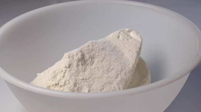woman adding one tablespoon of sugar to cottage cheese and flour in a white bowl. Close-up view of sugar being added for making cottage cheese pancakes