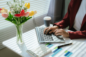 Businesswoman analyzing charts and financial data on laptop in modern office. She focuses on investment strategies and budget planning, collaborating with colleagues to drive organizational growth and