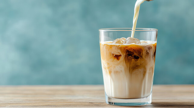 Creamy milk being poured into glass of iced coffee, creating beautiful swirl