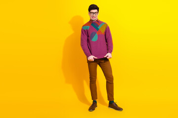Cheerful young man in a colorful sweater smiling confidently with hands posed against a vibrant yellow background.