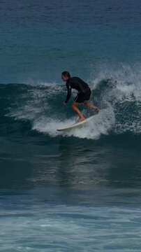 Male surfer ridding a wave under blue sky in a hot sunny day. Vertical slow motion video. Maldives