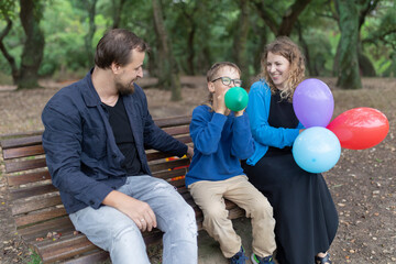Happy family inflating balloons in park: child blowing up balloon with parents