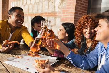 Happy friends toasting with beer bottles while eating pizza at restaurant
