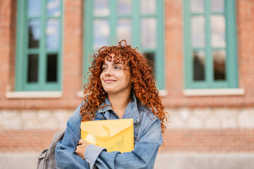 Smiling student holding a yellow envelope in front of university building