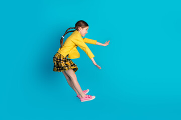 Obraz premium Young cute girl with braided hair in stylish outfit posing playfully against a bright blue background, radiating happiness, youthfulness