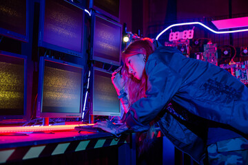 Asian woman wearing a black jacket hacking programming system and working with computer monitor...