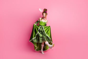 Fototapeta premium Elegant portrayal of a young woman in a green baroque gown on a pink background exuding historical charm with modern comparison.