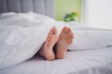 Bare feet peeking out from under a white blanket on a comfortable bed in a cozy and well-lit room...