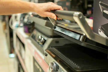 Buyer chooses electric grill while inspecting it in home appliance store.