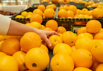 Abundance of oranges on counter in supermarket, hand of buyer takes fruit from crate close-up.