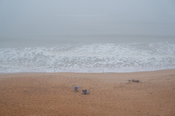 Cloudy beach day with fishermen near the shoreline surrounded by fog and waves crashing on the sand...