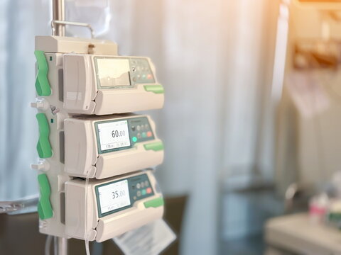 Medical infusion pumps with digital screens displaying flow rates in a hospital room. Close-up shot of intravenous therapy equipment. Healthcare and medical technology concept.