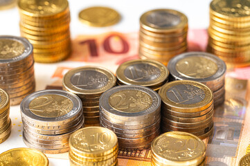 Stacks of coins next to each other, and banknotes, on white surface. Amount of money, currency and wealth.
