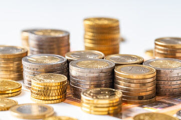 Stacks of coins next to each other, and banknotes, on white surface. Amount of money, currency and wealth.
