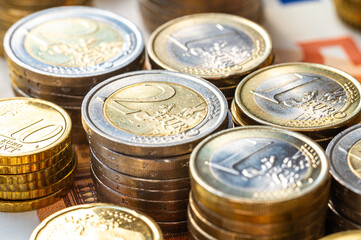 Stacks of coins next to each other, and banknotes, on white surface. Amount of money, currency and wealth.
