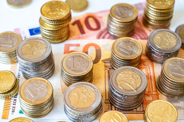 Stacks of coins next to each other, and banknotes, on white surface. Amount of money, currency and wealth.
