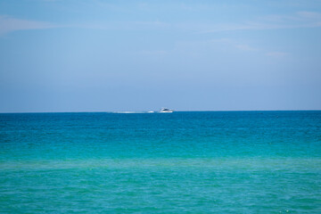 Fototapeta premium Calm turquoise waters and a distant boat enjoying a bright day on the ocean in a scenic coastal area